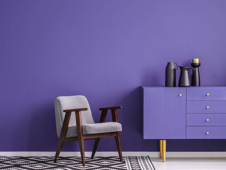 A wooden table with glasses, dishes, and candles in front of a dark purple wall.